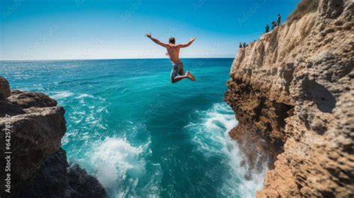 Man jumping into crystal blue water with camera on selfie stick.