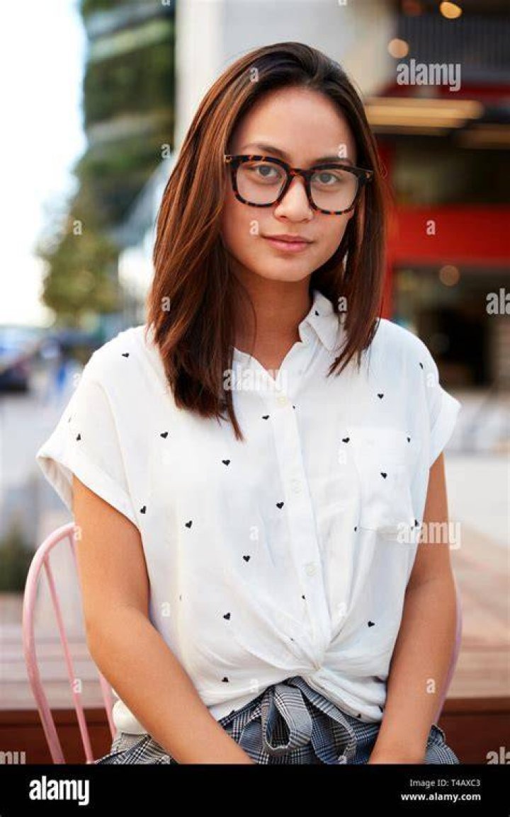 woman wearing glasses sitting with coffee, notes, and typing on a macbook.